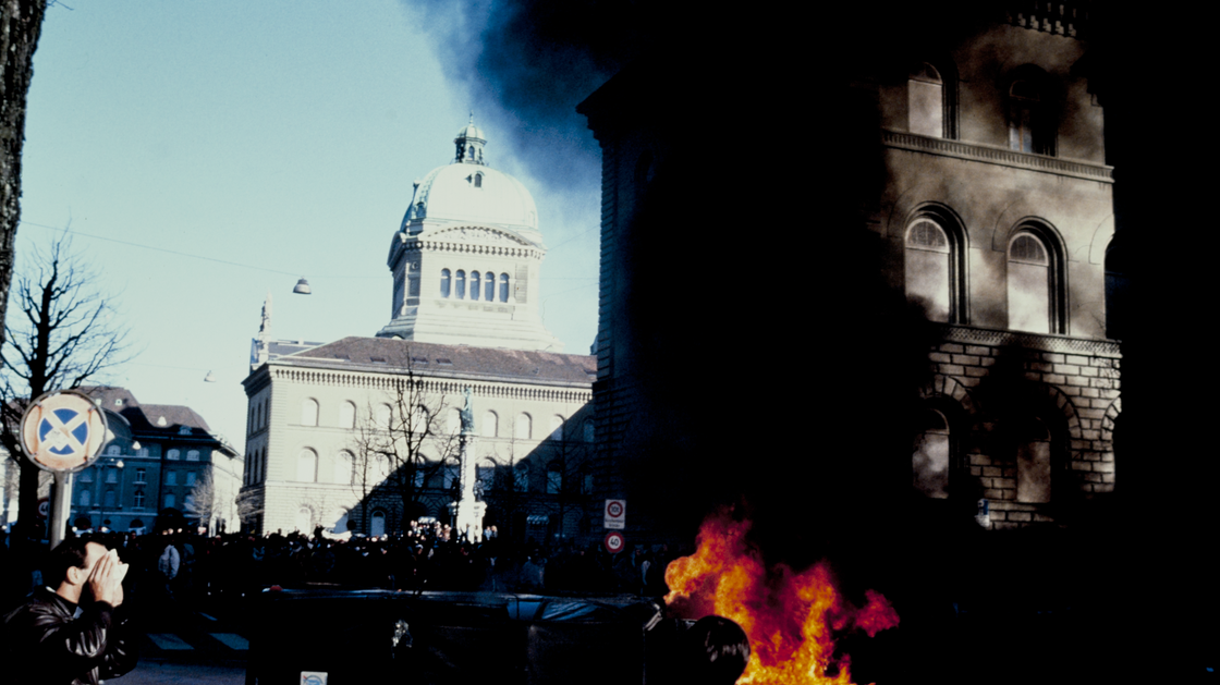 Fuoco e fumo durante la manifestazione contro gli interrogatori di Stato dei sospetti politici, con il Palazzo federale sullo sfondo